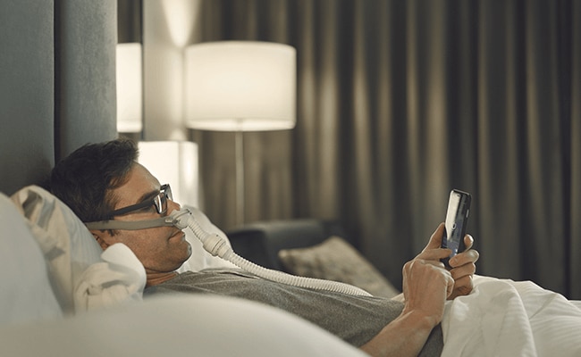 un monsieur dort avec son airmini à l'hôtel et son masque CPAP airfit p10