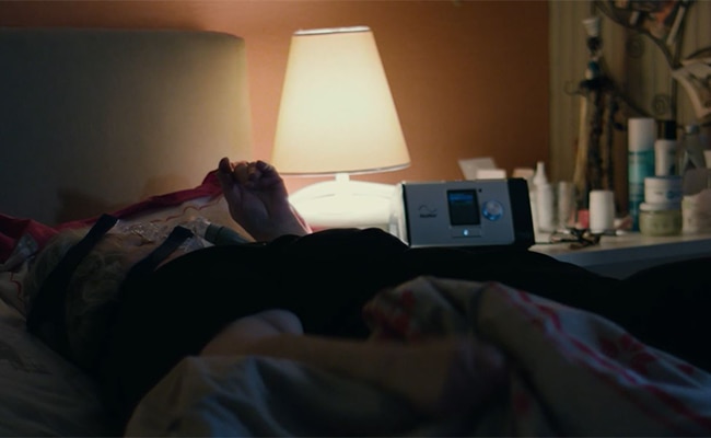 eine übergewichtige Frau trägt eine resmed-Maske, um im Schlaf besser atmen zu können