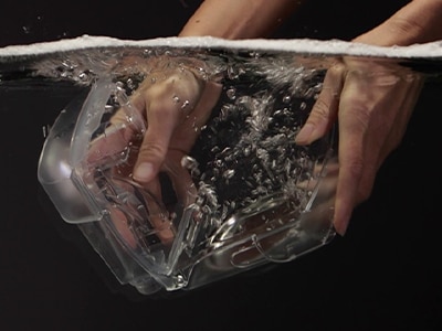 Une paire de mains plongeant dans l'eau un réservoir d’eau d'humidificateur d'un appareil CPAP ResMed sur fond noir.